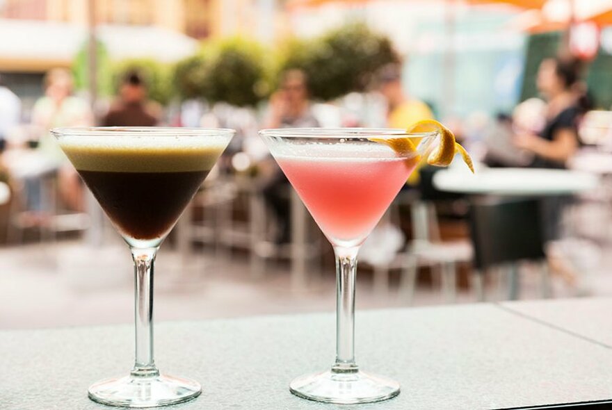 An espresso martini and a pink cocktail at a busy bar.