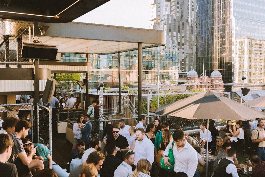 People enjoying drinks at a rooftop bar with cityscape in the background.