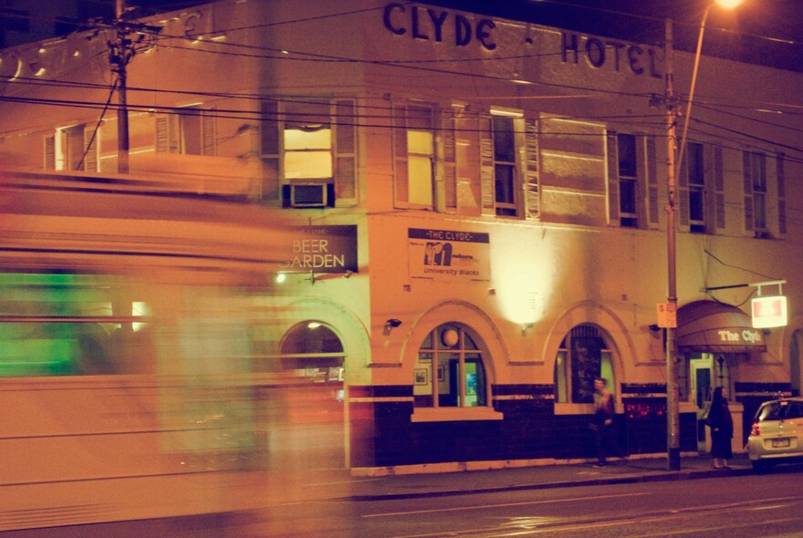 Blurred tram passing the Clyde Hotel at night.