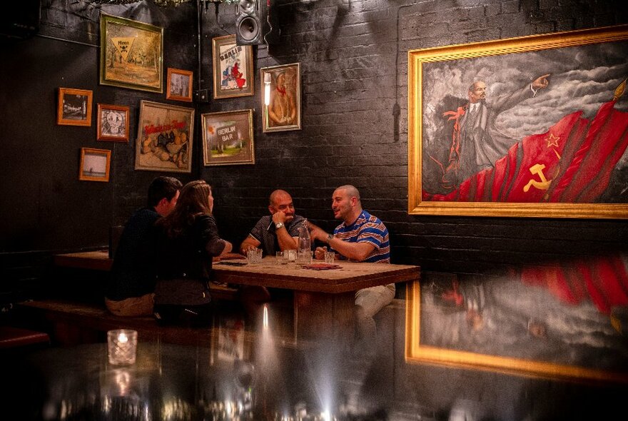 People seated at a table in a dark bar with walls lined with paintings.