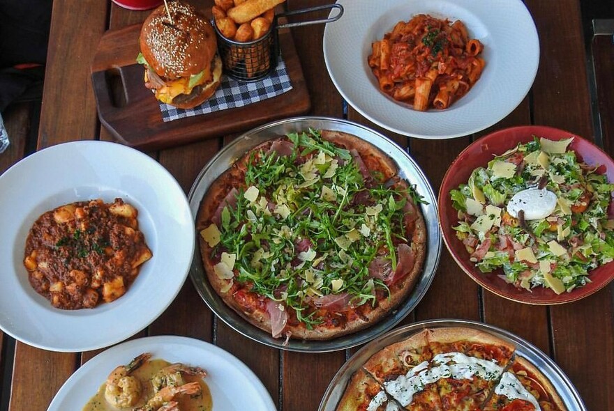 Assorted dishes on a table including hamburger with chips, pizza and salad.