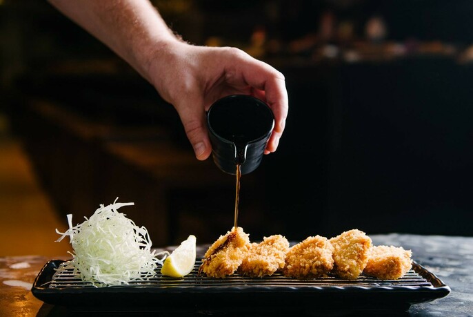 Sauce being poured on pieces of Japanese fried food.