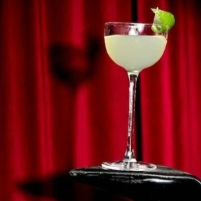 A cocktail with a lime garnish in front of a red curtain.