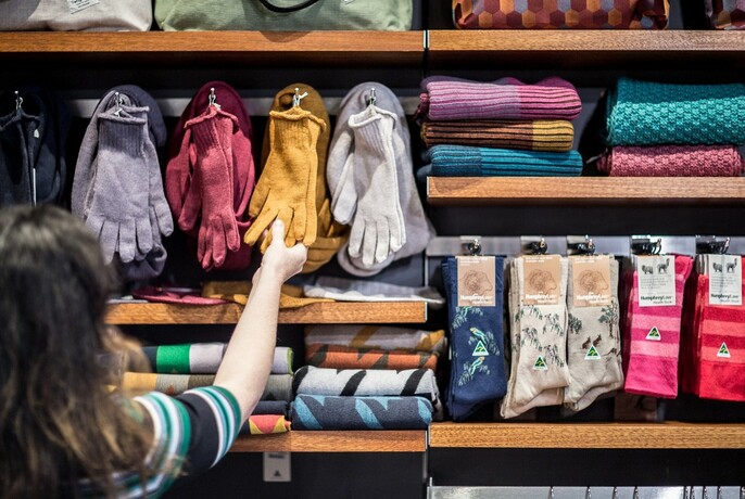 Customer selecting gloves from shelves displaying a range of clothes, including socks.