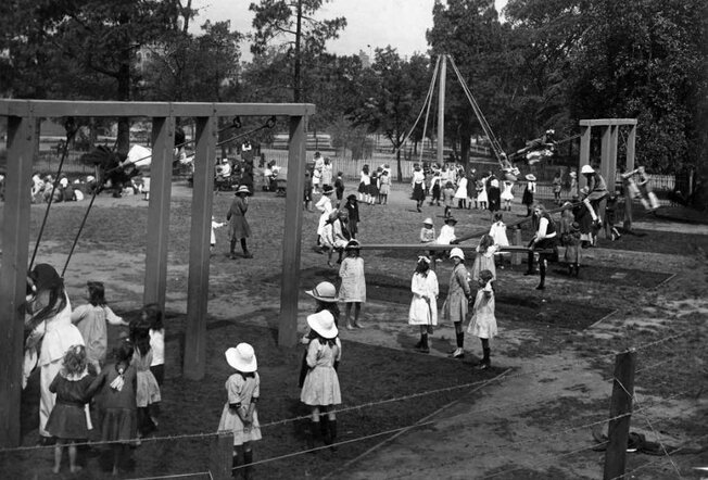 Black and white photo of children at the playground featuring swings and seesaws