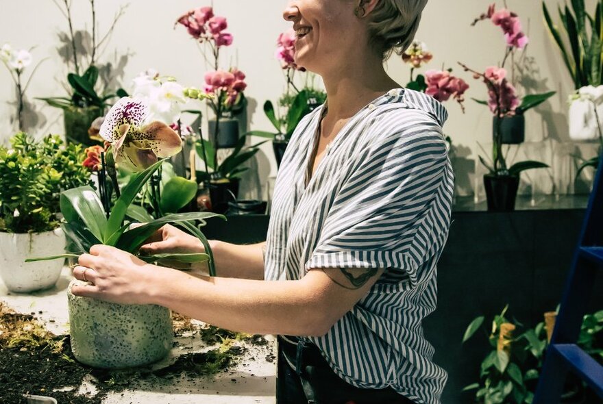 A smiling woman potting an orchid in a florist. 