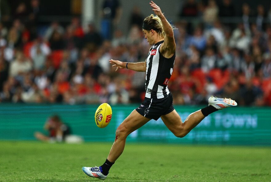 Collingwood AFL football player kicking a yellow ball on the field.