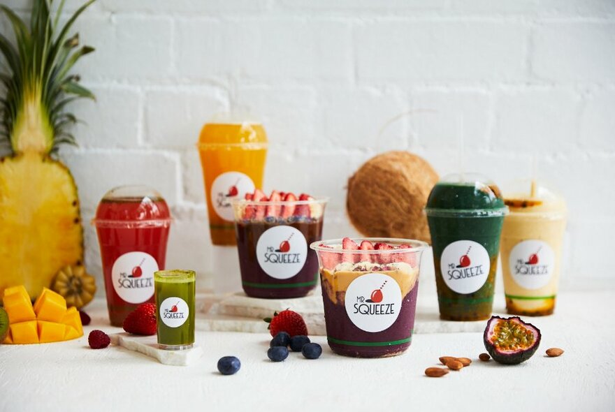 Selection of fresh pressed juices and smoothies in takeaway plastic cups on a white table.