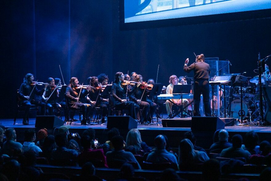 An orchestra playing on a stage with a conductor
