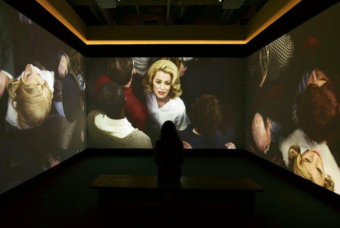 Gallery observer looking at a video projected onto three walls in a darkened room.