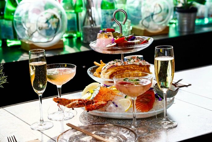 A tiered stand with lobster and more, with glasses of champagne and cocktails.