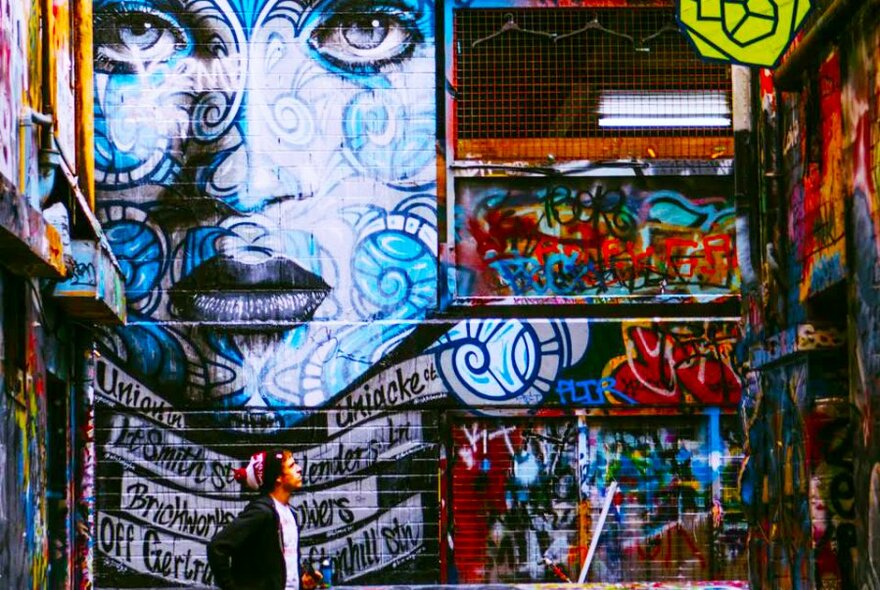 Man walking past the oversized street art portrait of a woman's face in a Melbourne laneway.