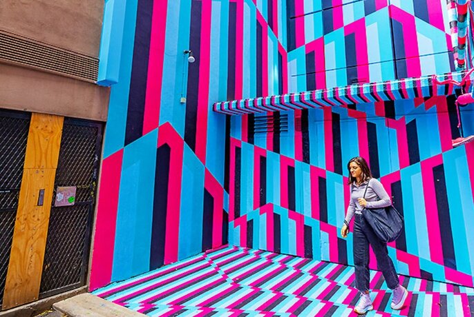 Person walking in a laneway that's painted in brightly-coloured stripes.