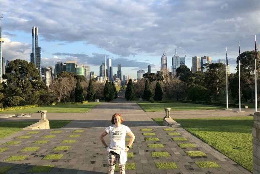 A smiling jogger standing in the sunshine with the city towers in the background.