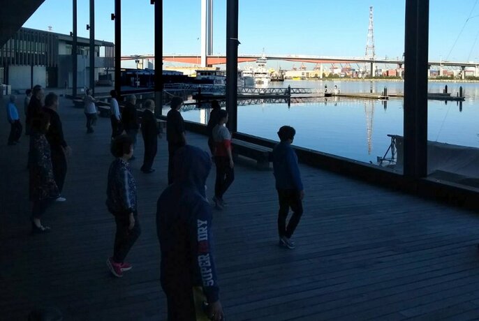 Tai chi class in shadow on a deck overlooking Docklands harbour.