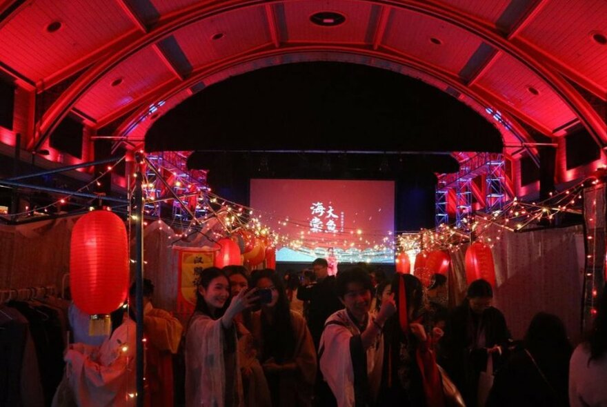 Red-lit auditorium with curved roof, with lanterns, lights and people taking selfies.