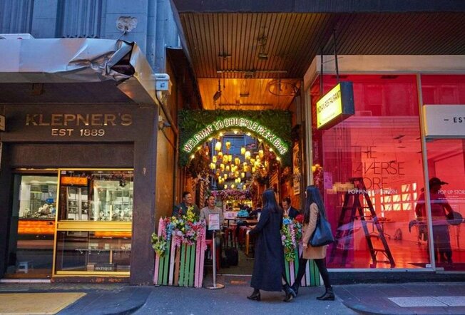 Two women walking into a tiny bar wedged between two retail stores