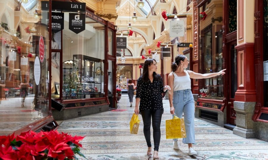 Two women with shopping bags in a shopping arcade with mosaic tiled floors.