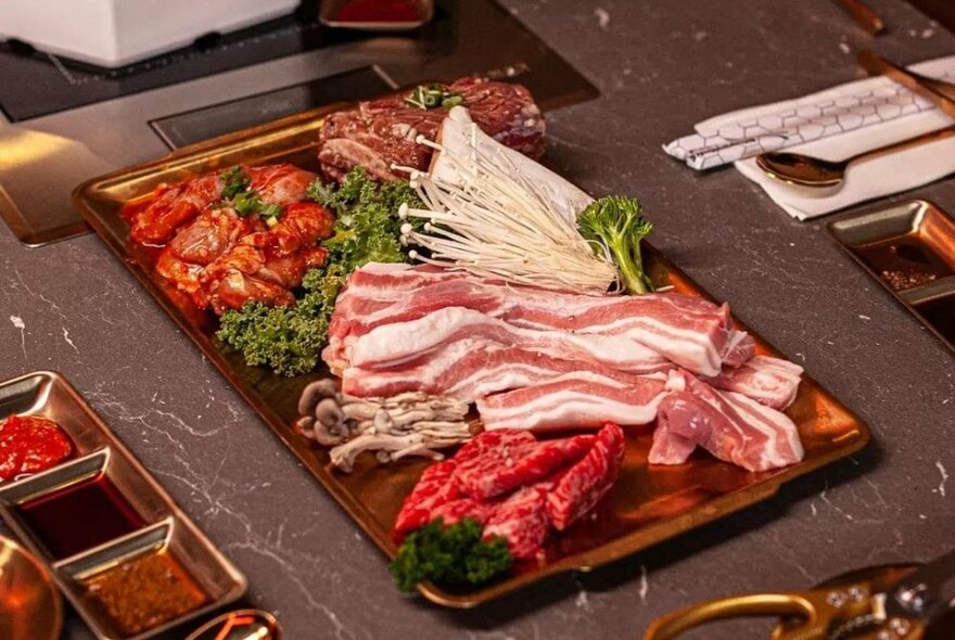 A plate of meats, seafood and vegetable waiting to be cooked on a table-top BBQ grill.