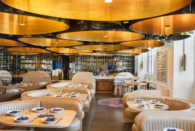 The sleek interior of Elchi restaurant, featuring large gold lights in the ceiling and semi-circular banquettes.