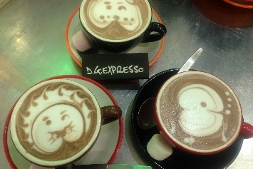 Three decorated coffees on a metal surface.