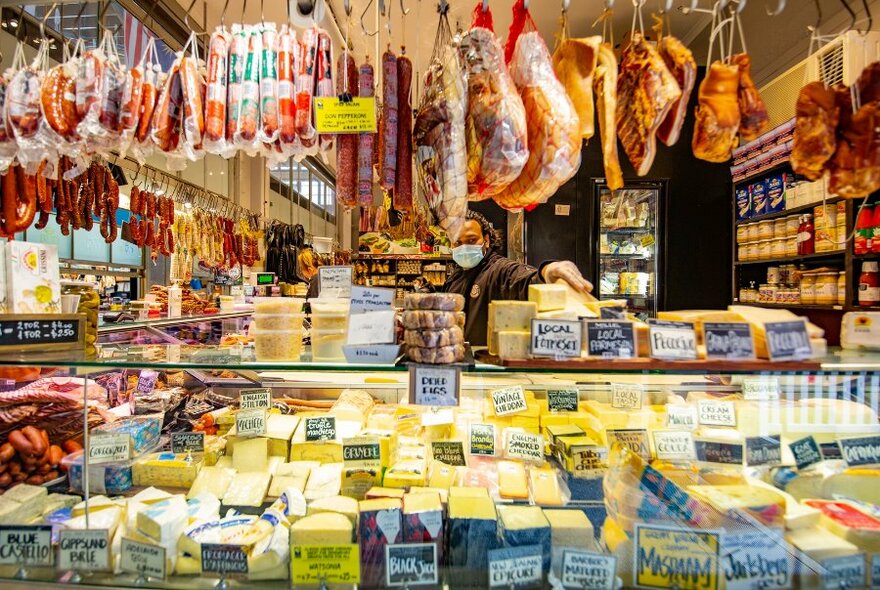 A market stall display with cured meats hanging from the ceiling and a huge glass case full of cheese