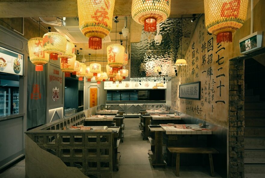 Interior of a restaurant showing booth style tables and chairs set for service, and many Chinese lanterns hanging from the ceiling.