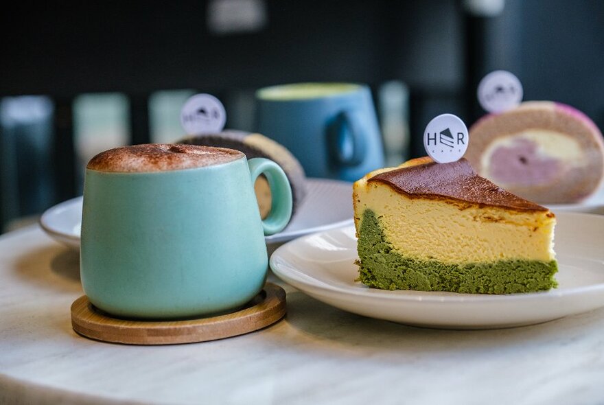 A mug of hot chocolate next to a layered yellow and green cake. 
