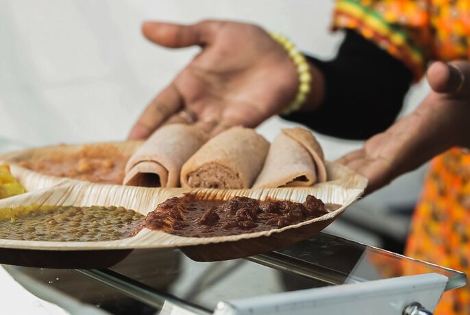 Hands holding out a tray of food that includes a meat and bean stew and rolled flat breads.
