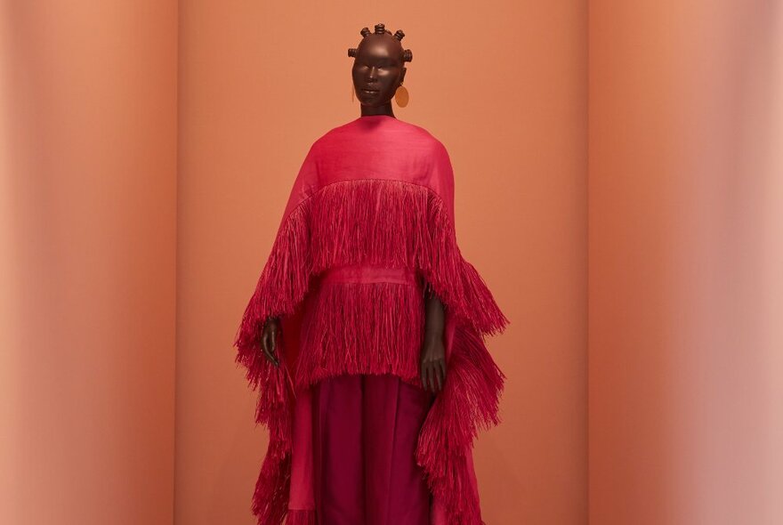 A mannequin wearing a red fringed dress, on display in a gallery room. 