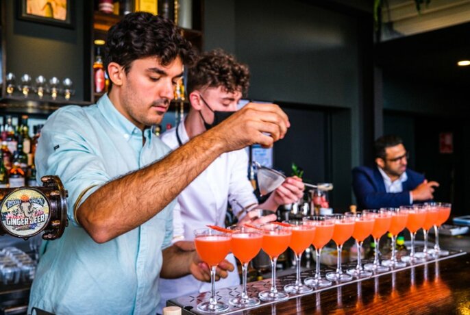 Two bartenders making a row of orange cocktails.
