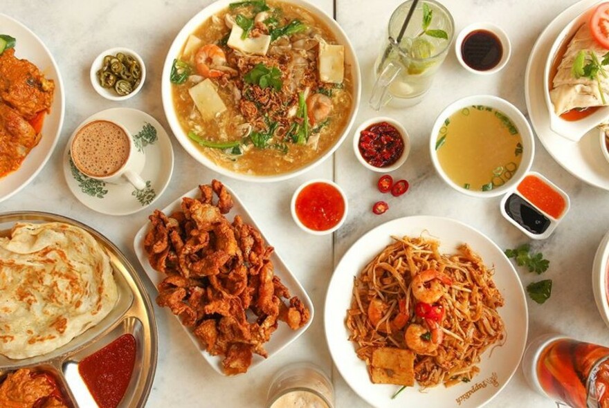Assortment of noodle and rice dishes with drinks and condiments.
