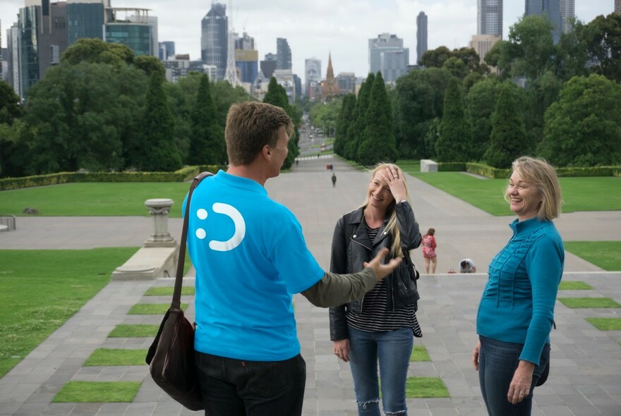Tour guide talking with two guests, with the city of Melbourne in background.