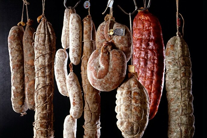 Various salami and cured meats hanging by string.