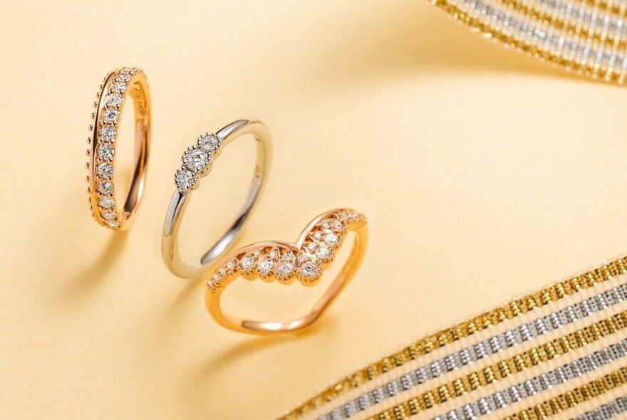 Three diamond rings on a yellow background with gold and silver ribbon.