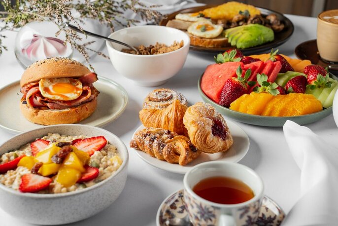 Breakfast dishes on a table, including granola, croissants, egg and bacon roll and fruit platter.