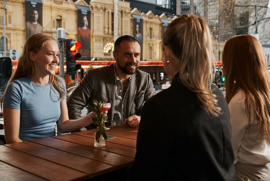People seated at an outdoor table with drinks and Melbourne's theatre district in the background.