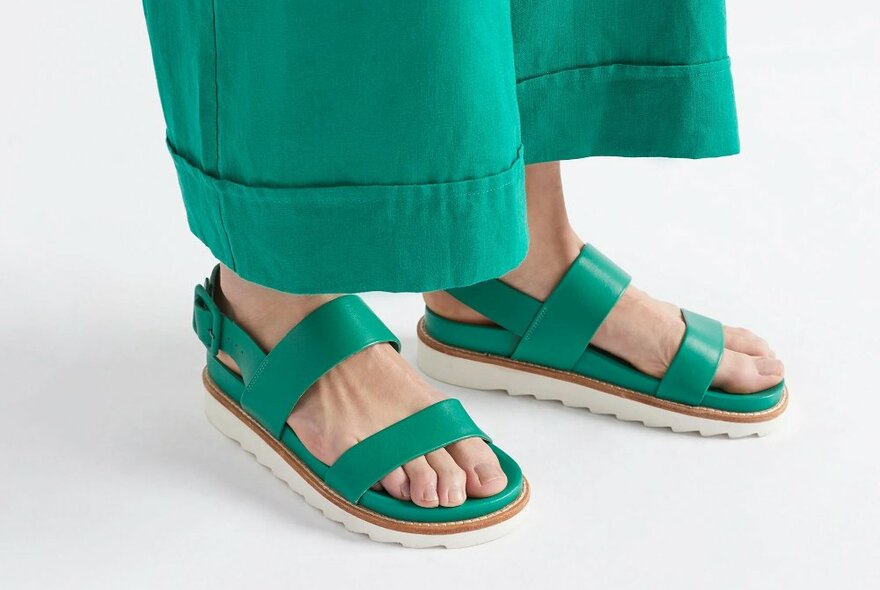 A model wearing a pair of chunky green sandals with green pants.