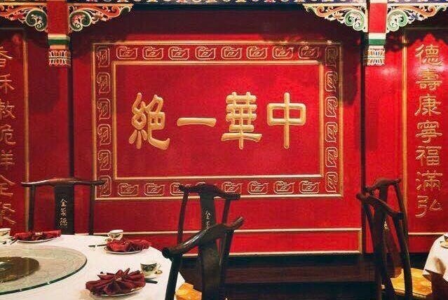 Red wall with gold Chinese script and details behind round table with black chairs.