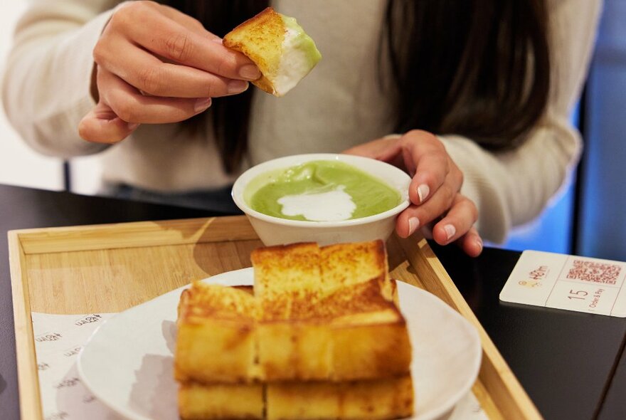 A person is dipping milk bread into pandan kaya dipping sauce