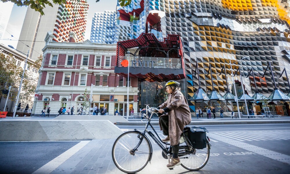 A cyclist riding a bike in front of the RMIT building. 