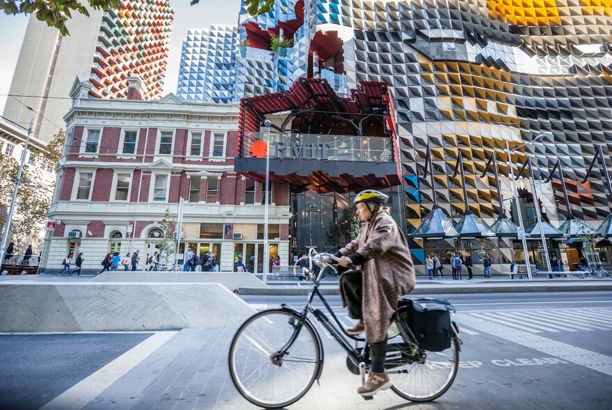 A cyclist riding a bike in front of the RMIT building. 