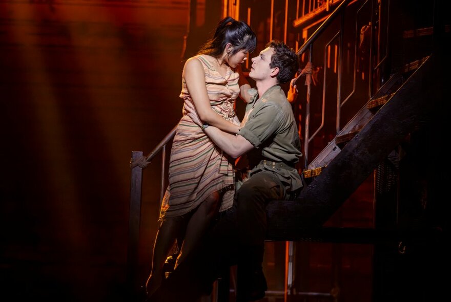 Two performers on a theatre stage, looking at each other intently and in a half embrace.