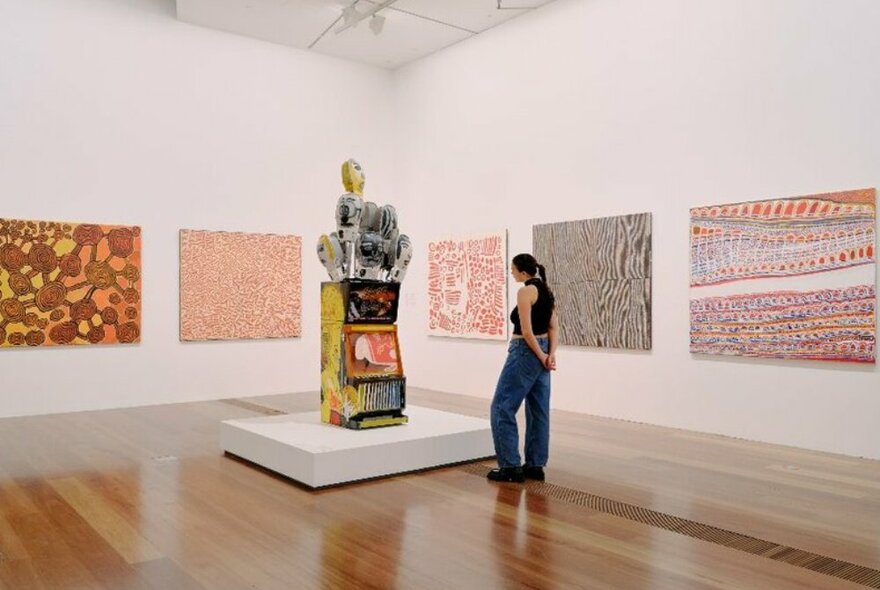 A woman looking at a large abstract sculpture in a gallery with Aboriginal traditional paintings on the walls.