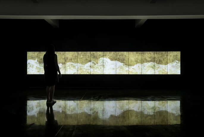 Person looking at an illuminated artwork in a darkened gallery.