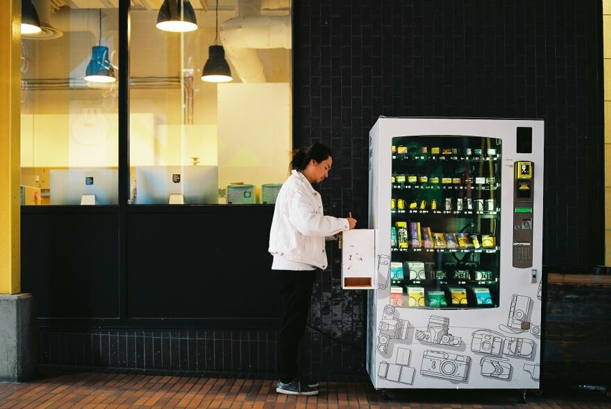 Person filling a vending machine on a street.