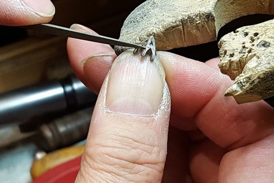 Fingers delicately working on a small piece of jewellery.