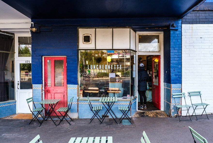 The exterior of a blue cafe with tables on the footpath and a red door.