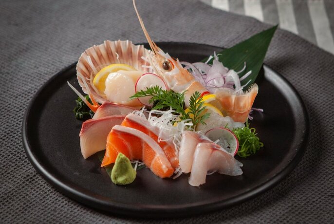 Sushi and sashimi arranged on a black plate.
