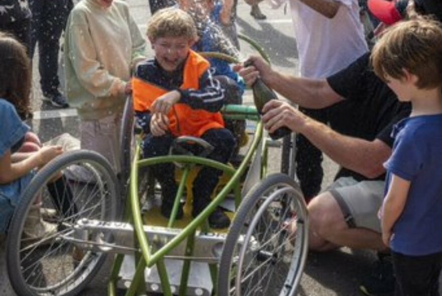 Child steering unpowered car, surrounded by other people.